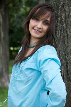 Portrait of young woman smiling by tree trunk