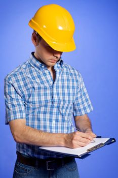 Architect in yellow hardhat writing on clipboard