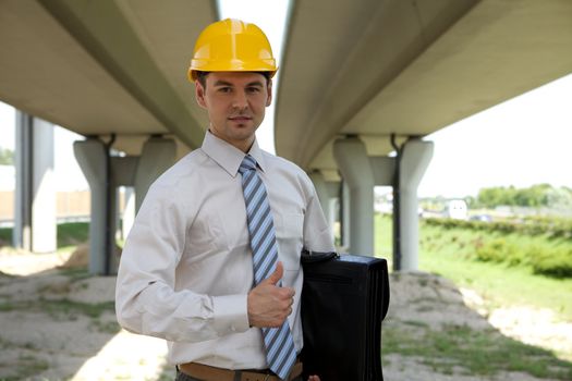 Portrait of architect in hardhat holding laptop bag and showing thumbs up sign