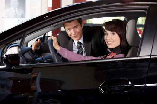 Portrait of young couple sitting in a new car at showroom