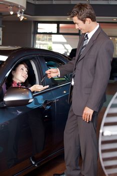 Car salesman giving the car keys to a young woman