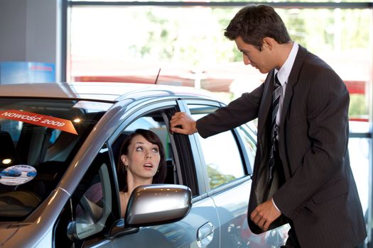 Car salesman conversing with female customer, sitting in new car
