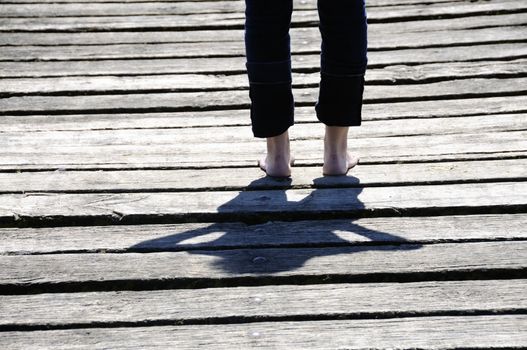 Young woman standing on wooden planks. Focus is on her shadow.