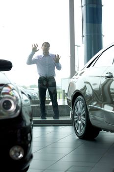 Young man curiously looking at new car in showroom