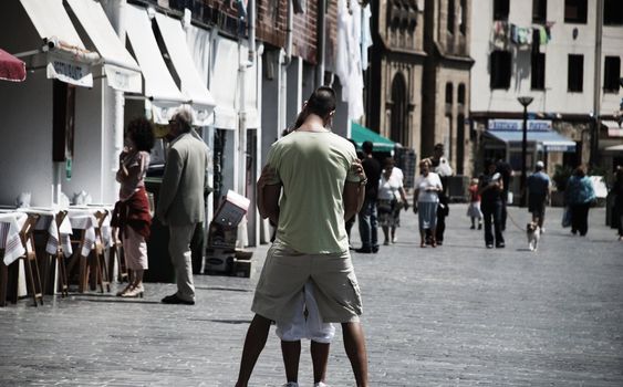 two teenagers are kissing and huging in the middle of a street in san sebastian.  people around them are walking. They are like in their own world just together.