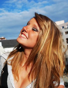 A blond young woman is laughing, with the blue sky in the background.