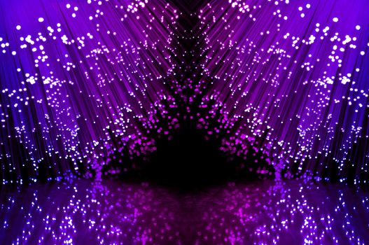 Close up on two groups of illuminated blue and magenta fiber optic light strands against a black background and reflecting into the foreground.