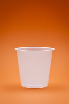 An image of a white empty plastic cup on an orange background