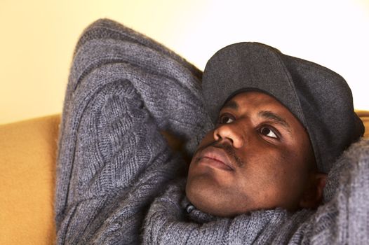 Portrait of a thoughtful young man of African descent with a cap lying on a sofa (Selective Focus, Focus on the left eye)