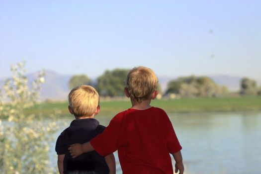 Two little brothers looking out towards water with protective arm extended.