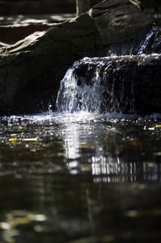 a sunlit waterfall and reflection into a calm pool against a rock background