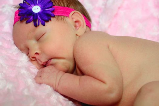 Newborn baby girl's first photo session asleep on pink blanket naked