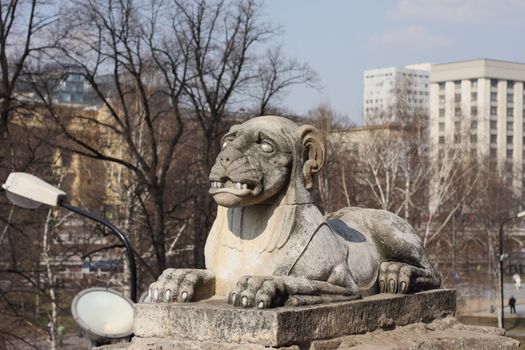 The sculpture, a lion, a monument, stone, a city, buildings, day, spring, trees, the sky, lays, a landscape