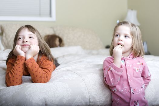 Two cute sisters watch television in their parent's bedroom.