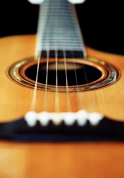 A very short depth-of-field image of an acoustic guitar from the bridge looking up the neck.
