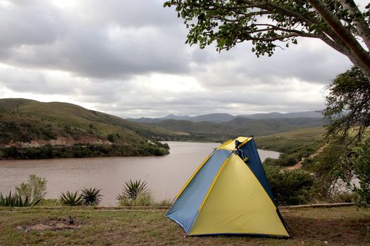 Small blue and yellow tent at a camping site next to a dam