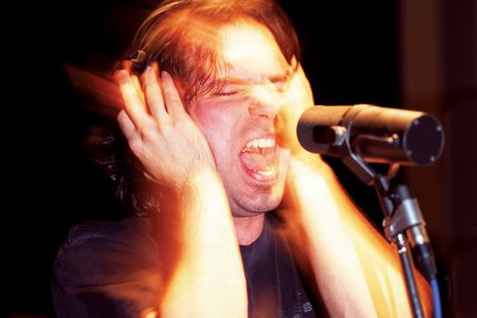 An aggressive music singer recording in a studio.  Lots of mood and atmosphere created with timed exposure with hand-held flash (some film grain because of the 1600 ISO film used)
