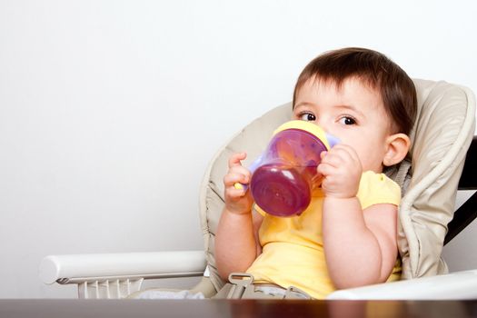Cute baby infant boy girl sitting in chair drinking from sippy cup.