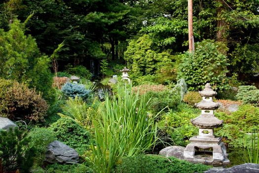 Beautiful peaceful Japanese zen garden used for meditation and relaxation, filled with green vegetation and granite Rokkaku Yukimi Lanterns.