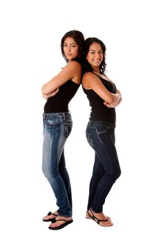 Two beautiful happy smiling young women standing together as a couple back to back, wearing blue denim jeans and blank tank tops, isolated.