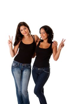 Two beautiful happy smiling young women couple friends making peace victory gesture with fingers while hugging each other, wearing black tank top and blue denim jeans, isolated.