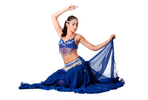 Beautiful Israeli Egyptian Lebanese Middle Eastern belly dancer performer in blue skirt and bra with arm in air sitting with eyes closed, isolated.