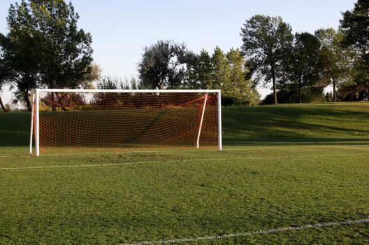 A soccer net with shot in bright sunlight with trees in the background.
