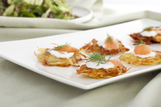 Bite sized potato rosti appetizer topped with fresh sour cream, smoked salmon and dill.