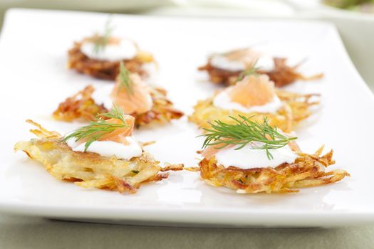 Bite sized potato rosti appetizer topped with fresh sour cream, smoked salmon and dill.