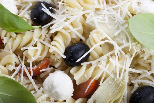 Close up of pasta salad with basil, olives, tomatoes, and fusilli. 
