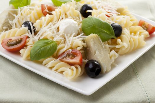 Fusilli pasta with black olives, mozzarella cheese, artichoke hearts and tomato slices, topped with fresh basil leaves. 