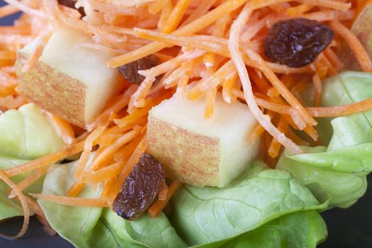 Close up of fresh carrot salad with raisins and apples on a bed of lettuce