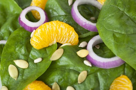 Close up of mandarin spinach salad with red onions and sunflower seeds.