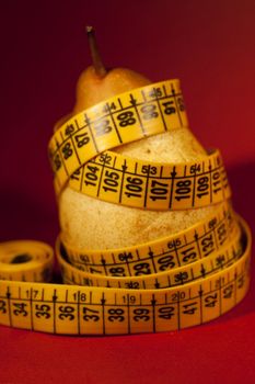 Close view of a pear with measuring tape over a red background.