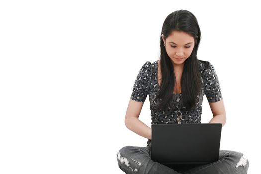 beautiful young female student sitting on floor studying on a laptop, isolated on white