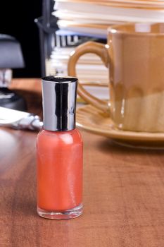 Orange nail polish standing on a table in front of a coffee cup.