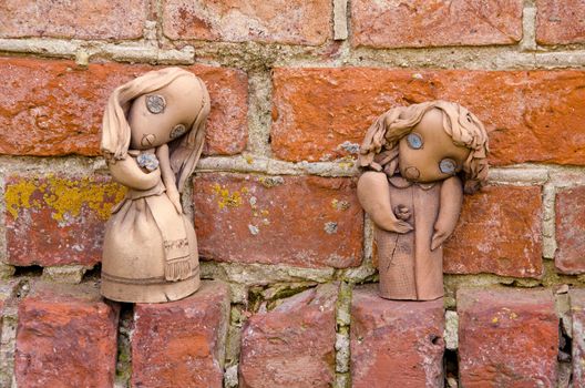 Handmade women figures made of clay on background of red brick wall.