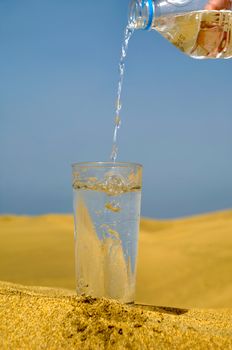 A glass of fresh water and bottle in a desert. Note that the water and bubbles are in motion blur.