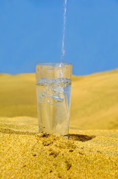 A glass of fresh water and bottle in a desert. Note that the water and bubbles are in motion blur.