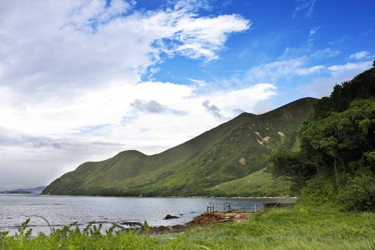 Green grass on sea coast under blue sky and mountain