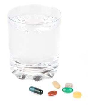 Various pills with glass of water on a white background