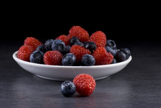 Plate of fresh blueberries and raspberries on balck background