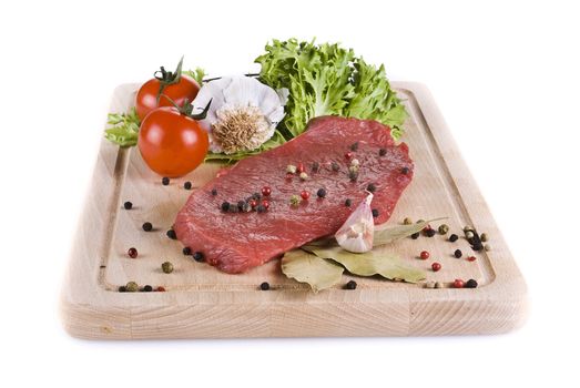 Raw beef frying steak on chopping board with vegetables isolated over white background