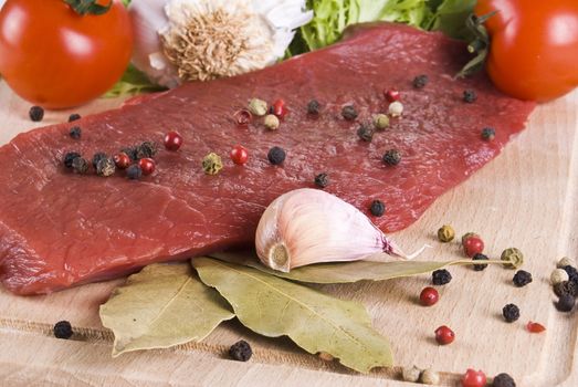 Raw beef frying steak on chopping board with vegetables