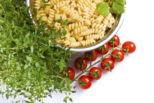 Fusilli pasta in colander with thyme and tomatoes over white background