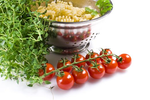 Fusilli pasta in colander with thyme and tomatoes over white background