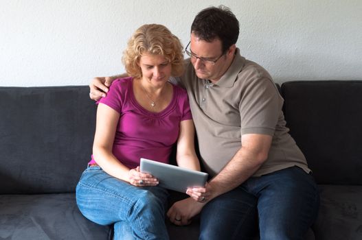 Middle-aged couple sitting comfortably on a sofa and checking a digital tablet pc