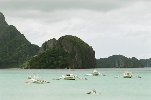 Yacht and outrigger boats that are anchored on the calm water, photos taken in El nido, philippines