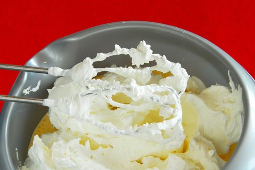 mixer whisks with white cream whipped over silver bowl