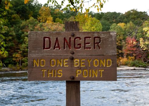 Wooden painted danger sign by rushing river